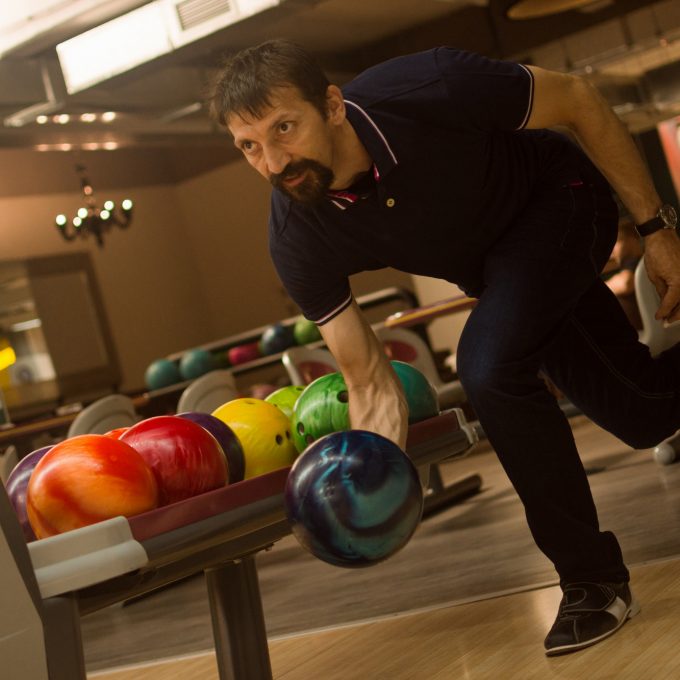 The male player is playing bowling in the bowling club.